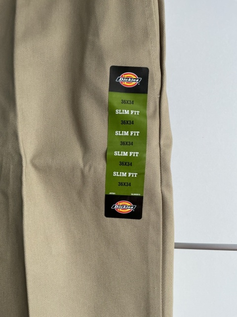 Zbliżenie na materiał i metkę Dickies na beżowych spodniach męskich